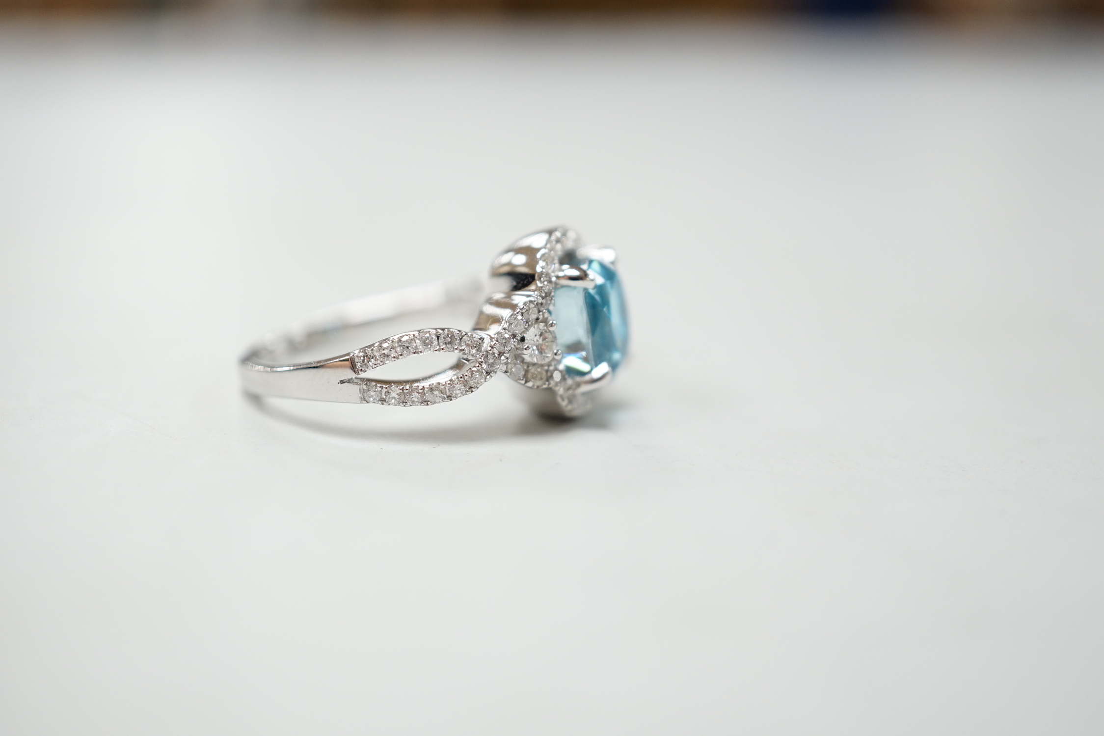 A modern 14k white metal, cushion cut blue zircon and diamond chip set cluster dress ring, with diamond chip set shoulders, size O, gross weight 6.8 grams.